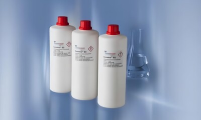 Drei weiße Reagenzienflaschen aus Plastik, jede mit einem roten Schraubverschluss versehen, sind in einer Reihe angeordnet.
